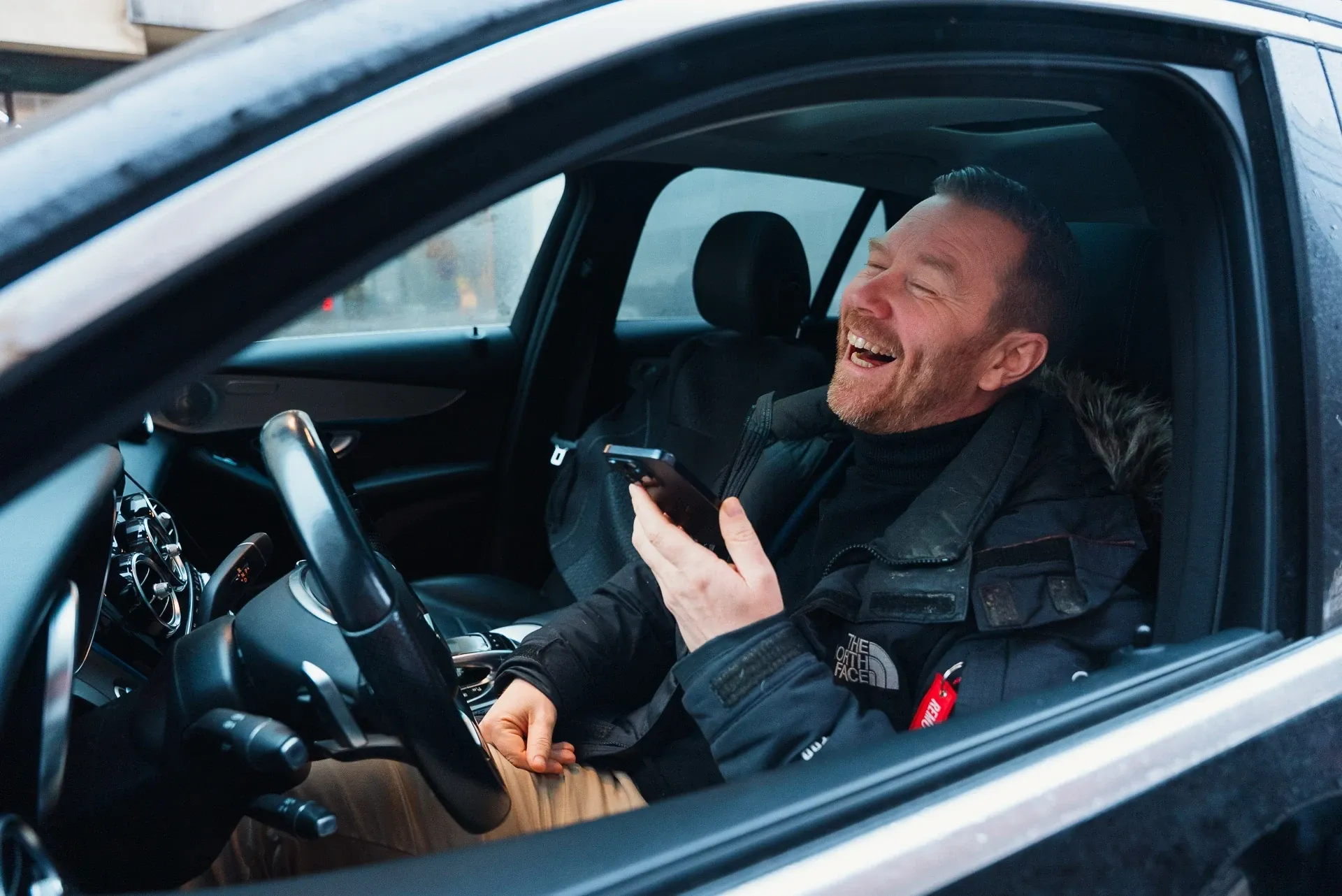 Mies nauraa autossa ja sanelee matkalaskun puhelimeen